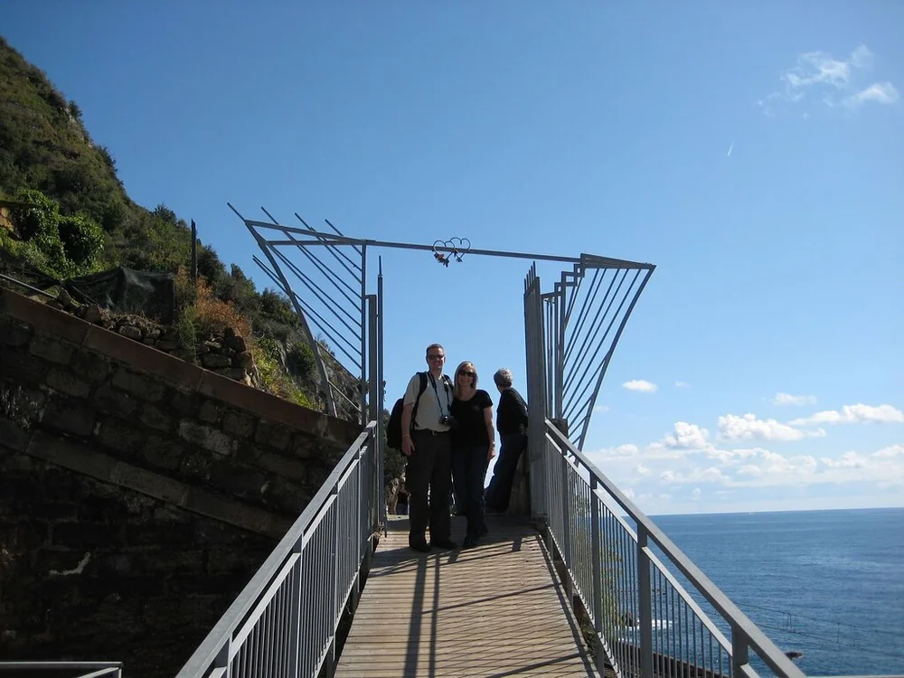 Walkers on a metal walkway under an arch with a heart ornament above the sea