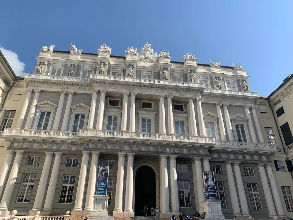 The ornate white facade of a grand palazzo in Genoa under a blue sky
